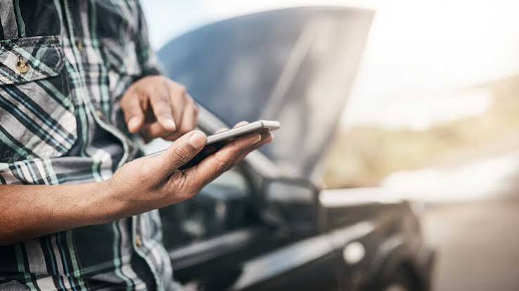 Driver using a smartphone in front of an open car hood