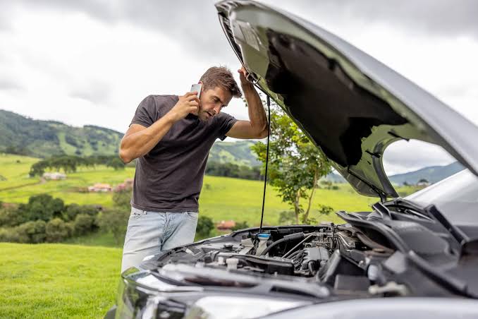 Driver on the phone looking under the hood of a stopped car