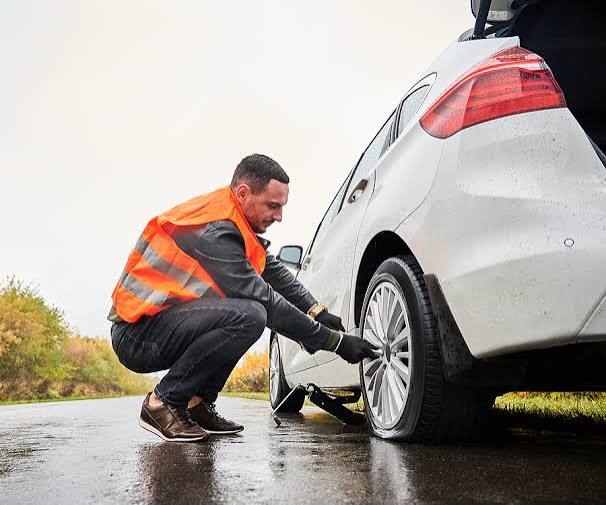 Easy To Plug technician in a safety vest changing a tire on a white car