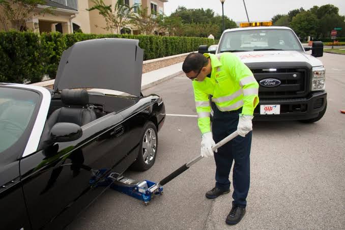 Technician using a floor jack to lift a vehicle for a roadside tire change